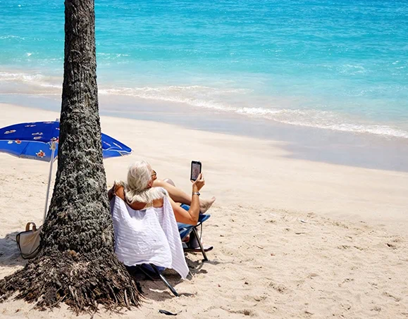 Person relaxing in beach chair under palm tree on a white sand beach in Kona, Hawaii